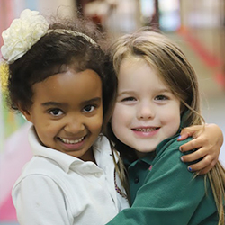 Two young students smiling together with their arms around each other.