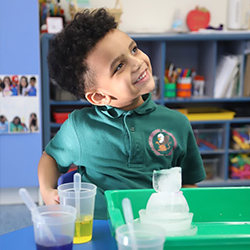 Child smiling while playing with messy sensory materials outdoors.