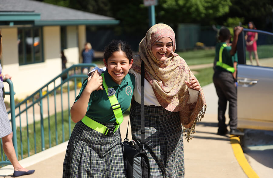 Learn more about Westminster School Two students smiling together outside during school drop-off.