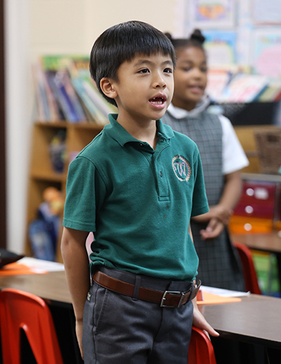 Lower School Homepage Lower school boy in classroom wearing Spring uniform.