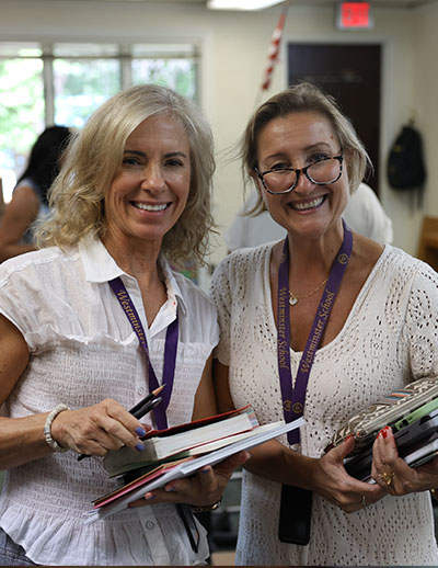 Two teachers holding materials and books smiling