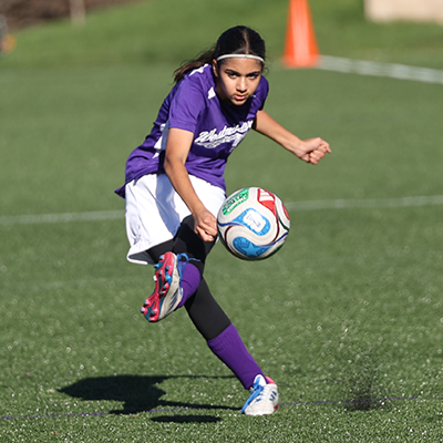 Girl kicking soccer ball turf flying in air