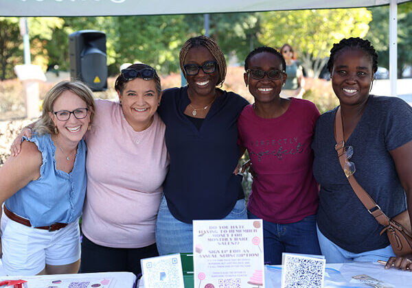 how to apply photo 2 Group of smiling people standing together behind an information table at a school event.