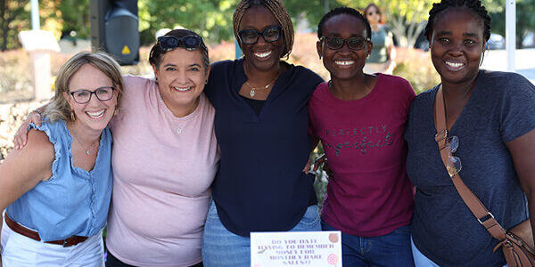 how to apply photo 2 Group of smiling people standing together behind an information table at a school event.